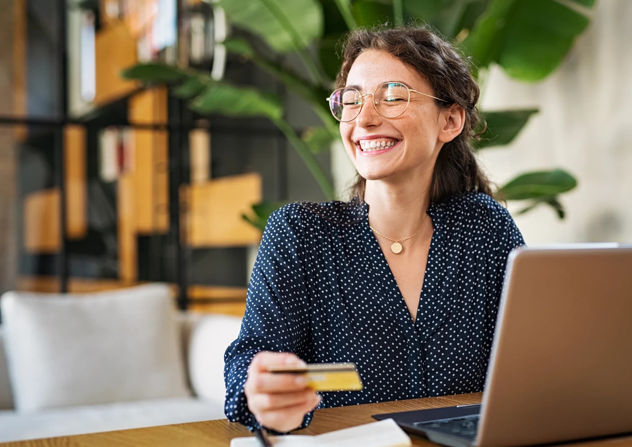 A smiling woman holding her card in front of a laptop